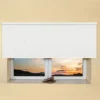 White light filtering roller blind fitted above a recessed window, with a sunset view