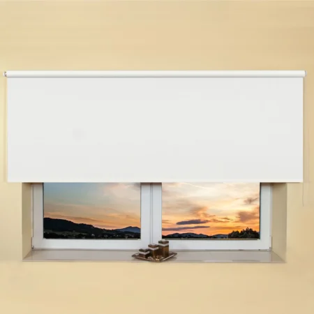 White light filtering roller blind fitted above a recessed window, with a sunset view